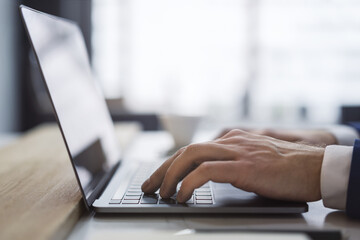 Poster - The picture captures a man's hands up close as they type on a sleek laptop keyboard, with an office setting appearing blurred in the background