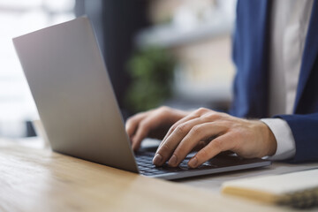 Poster - In the photo, male hands are captured in close detail, typing on a modern laptop keyboard, with a softly blurred office setting in the background