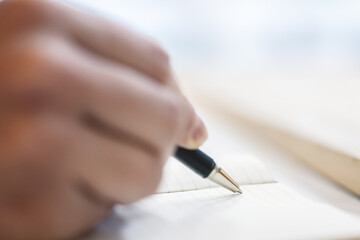 Poster - A man's hand seen in close-up, writing in a notepad, against a soft-focus backdrop