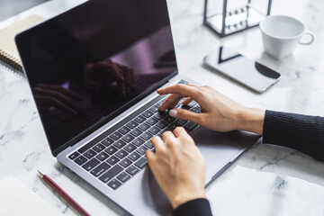 Poster - A woman's hands typing on a sleek laptop keyboard, with the office environment appearing hazy in the background