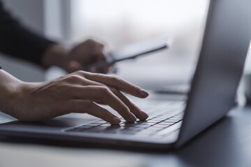 Wall Mural - A close observation of a woman's hands actively typing on a sleek laptop keyboard, set against a fuzzy office backdrop