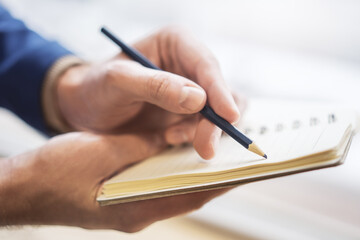 Poster - Focused view of a man's hand as he writes in a notepad, background gently blurred