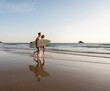 © Westend61 - Young couple running on beach, carrying surfboard