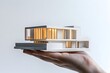 © Agri - A Hand Holding a Miniature Model of a Modern Home with Illuminated Windows