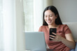 © PheelingsMedia - Happy asian woman using multiple devices sitting in a sofa