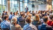 © engincan - Rear view of a diverse audience engaged in listening to a speaker delivering a presentation at a business conference hall