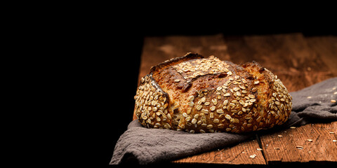 Fototapete - Artisan wheat oat bread on a wooden table on black background. Panoramic view, free space for text