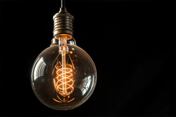 Poster - A round vintage-style light bulb is suspended against a completely black background. 