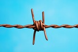 A rustic barbed wire fence stretching across an open prairie under a vast blue sky, with a few tufts of grass swaying in the wind