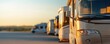 © ParinApril - A row of recreational vehicles parked during sunset, showcasing their sleek designs and warm lighting.