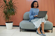 © Seventyfour - Full length shot of concentrated female SEO analyst in smart casual outfit typing on laptop, while working on comfy seat in lounge area of modern coworking space