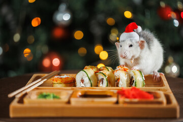 Poster - A colorful rat in a red Santa hat celebrates the New Year. A Christmas tree with a blinking garland and balls. Sushi and rolls on a wooden festive table. Asian cuisine on holiday.