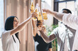 © BullRun - Happy company toasting beer bottles in brightly lit apartment