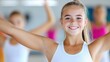 © svastix - A young girl smiles brightly while posing in a dance class, wearing a white outfit as others in colorful costumes form the blurred background of the studio environment.