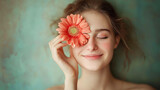 Portrait of a happy young woman holding Gerbera daisy covering her eye with eyes closed