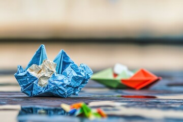 Aufkleber - A blue paper boat sits on the surface of a small puddle of water