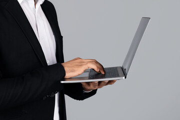 Poster - Cropped of entrepreneur stands in a studio environment, focused on typing on a laptop. Dressed in formal attire, he represents a modern, corporate lifestyle.