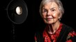 © imagineRbc - A smiling elderly woman with silver hair wears a floral shirt and shawl while being lit by a studio light. The background is dark, creating a striking contrast