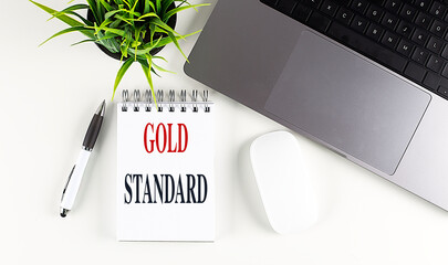 Poster - Gold standard written on a notepad with a laptop, pen, mouse, and green plant on a white desk