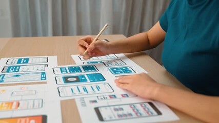 Startup company employee planning for user interface prototype for mobile application or website in office with model of program on desk. UX UI designer consider user friendly interface plan. Synergic
