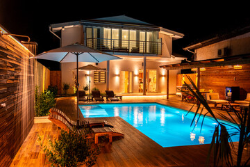 Luxury house with illuminated swimming pool and wooden deck at night. Concept of modern outdoor living space