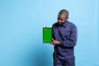 © DC Studio - Skilled guarding agent shows isolated mockup screen on tablet, holding chromakey display against blue background. Security officer posing in work uniform with baton on camera.