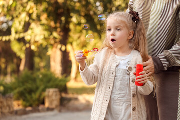 Poster - Little girl with her mother blowing soap bubbles in park on autumn day