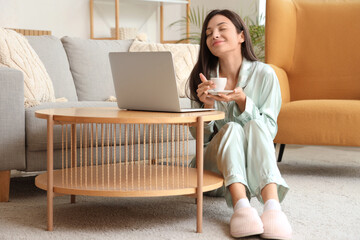 Wall Mural - Young woman in green pajamas working with coffee and laptop on table at home