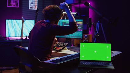 Fototapete - Musician mixing and mastering sounds at home studio with electronic console and soundboard, creating modern tunes. Sound engineer producing audio tracks with greenscreen on tablet. Camera B.