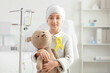 © Pixel-Shot - Little girl with yellow ribbon and toy bear undergoing chemical therapy course in clinic. Childhood cancer awareness concept