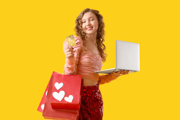 Wall Mural - Young woman with laptop and credit card shopping online on yellow background. Valentine's Day celebration