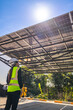 © ultramansk - Engineer in safety vest and helmet pointing towards a solar powered carport, illustrating eco-friendly innovation in parking infrastructure. Solar panels provide shade and sustainable energy.
