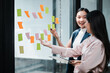 © Satori Studio - Two businesswomen brainstorming with sticky notes on a glass wall, showcasing teamwork and creativity in a modern office environment.