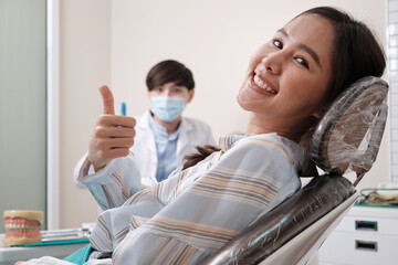 Wall Mural - Young beautiful female patient with male Asian dentist, examine teeth stomatology in dental clinic, well-being hygiene checks, and professional orthodontic healthcare work in doctor's office hospital.