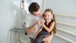 © Mariia - A loving father is holding his daughter in the arms and helping her brushing their teeth in a bathroom.