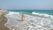 © fotoworld - A woman of Caucasian ethnicity enjoys the ocean waves on a sunny beach, capturing the essence of summer relaxation