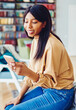© BullRun - Pretty black female millennial typing text for sending mobile sms during web communication in loft apartment, attractive Generation Y with dark skin updating notification for smartphone application