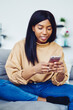 © BullRun - Dark skinned woman enjoying online messaging on modern cellphone technology during weekend leisure in home apartment with cozy interior, African American blogger 20s networking social wireless