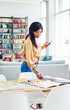 © BullRun - Youthful female freelancer checking papers on desktop during weekend time in cozy home apartment, African American woman holding modern smartphone technology standing near table in loft flat
