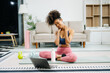 © Nuttapong punna - Woman Doing Yoga and Watching Online Tutorials on Laptop, Training in Living Room at home