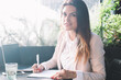 © BullRun - Portrait of smiling caucasian businesswoman writing information making research for project on freelance, beautiful female author satisfied with remote job process on cafe terrace creating article