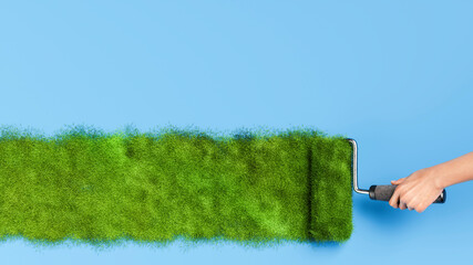 Hand painting green grass with paint roller on blue background