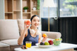 © laddawan - wellness as a cheerful woman enjoys a salad and fruits while engaging with technology at home