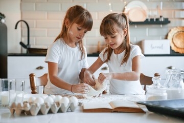 Flour and eggs on the table. Two little girls are preparing food on the kitchen with garlands