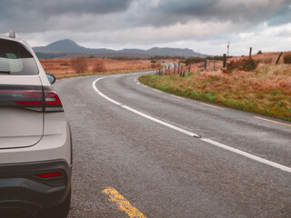 Fototapete - White color family car parked off small narrow road on a bend. Beautiful rough landscape with fields and mountains in the background. Travel in rented car concept. Sightseeing in Connemara, Ireland.