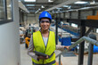 © 24K-Production - Female industrial plant employee with a blue helmet and yellow vest in a business factory. Manufacturing, labor, and women concepts.