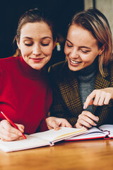 Fototapete - Successful two hipster girls drawing design sketch for new project teamworking in coffee shop.Cheerful friends writing down common plans of collaboration in notepad resting together in coworking