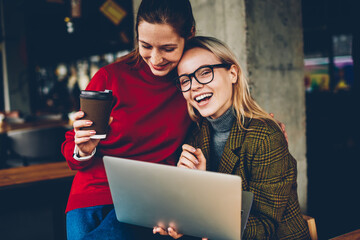 Fototapete - Portrait of happy blonde female blogger laughing at camera while having fun with best friend enjoying communication with each other and watching funny video on websites on laptop with 4G internet