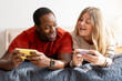 © Maria Vitkovska - Happy middle aged couple having fun playing online using mobile phones in bedroom