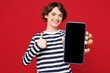 © ViDi Studio - Young smiling satisfied happy woman she wear blue striped sweatshirt casual clothes hold in hand use mobile cell phone show thumb up isolated on plain red background studio portrait Lifestyle concept